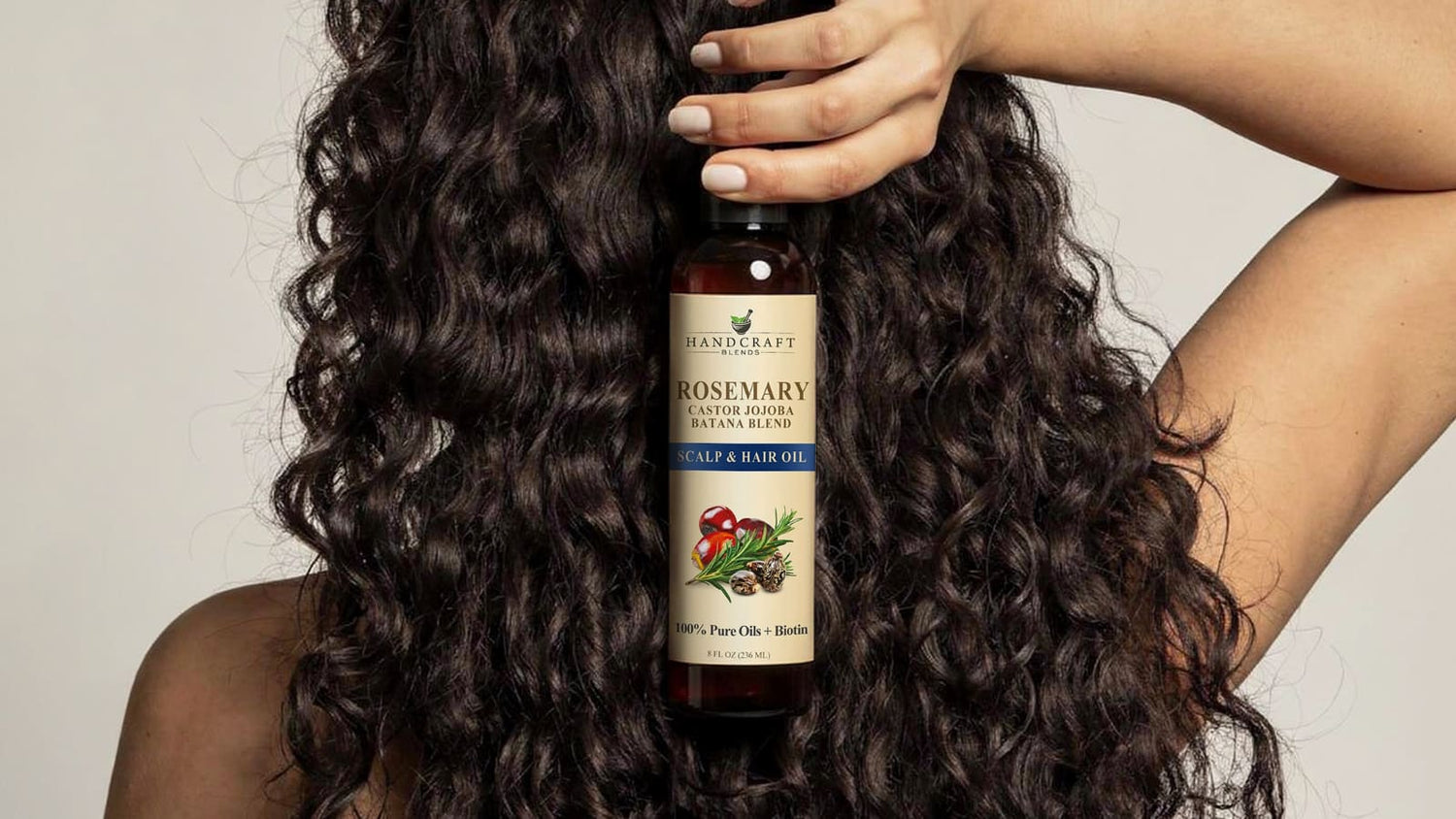 Person with curly hair holding rosemary castor jojoba scalp and hair oil bottle