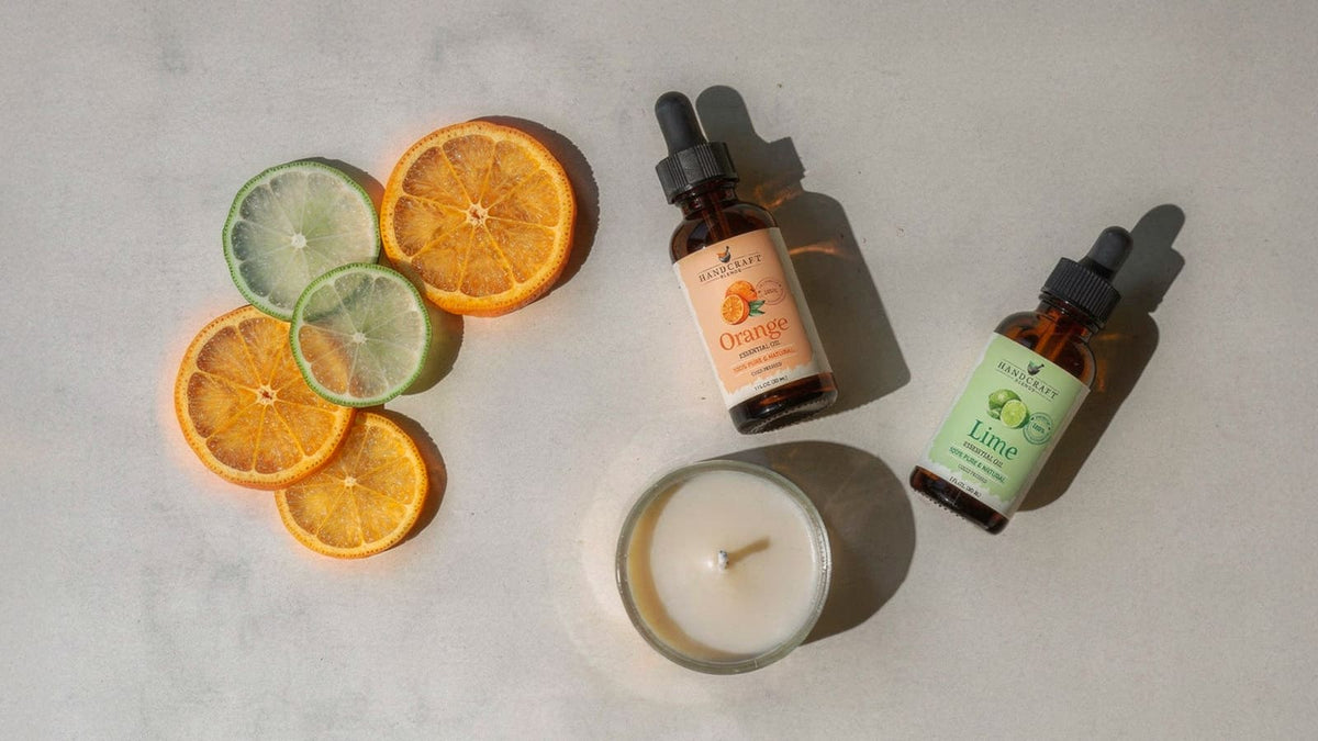 Freshly poured citrus candles with orange slices, grapefruit peel, and amber essential oil bottles on a bright counter