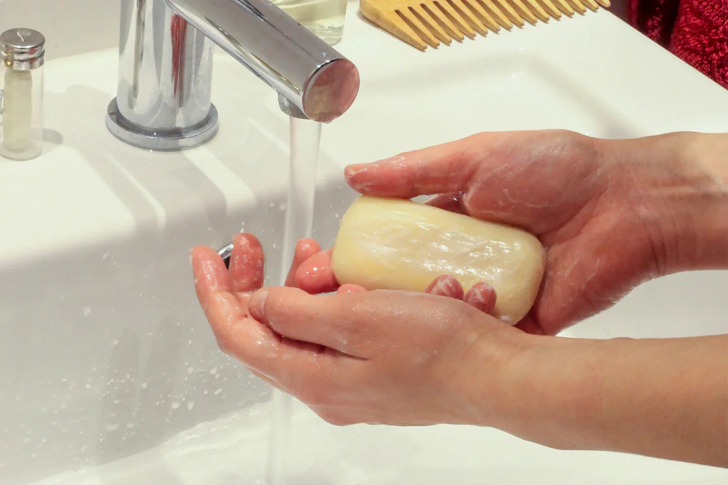 Hands washing with a natural bar soap under running water at a bathroom sink