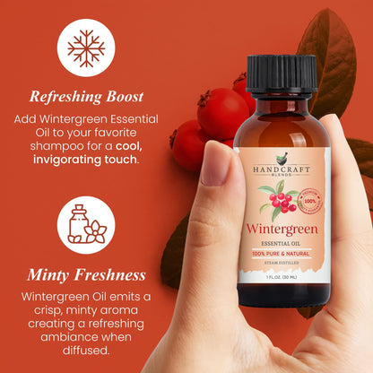 Hand holding a bottle of wintergreen essential oil with berries and leaves on an orange background